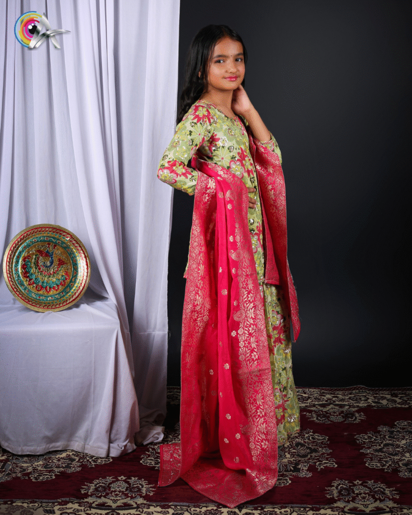 Child model in traditional Indian attire with floral designs, hand on her waist and dupatta draped over her arm, giving an elegant pose against a studio backdrop.