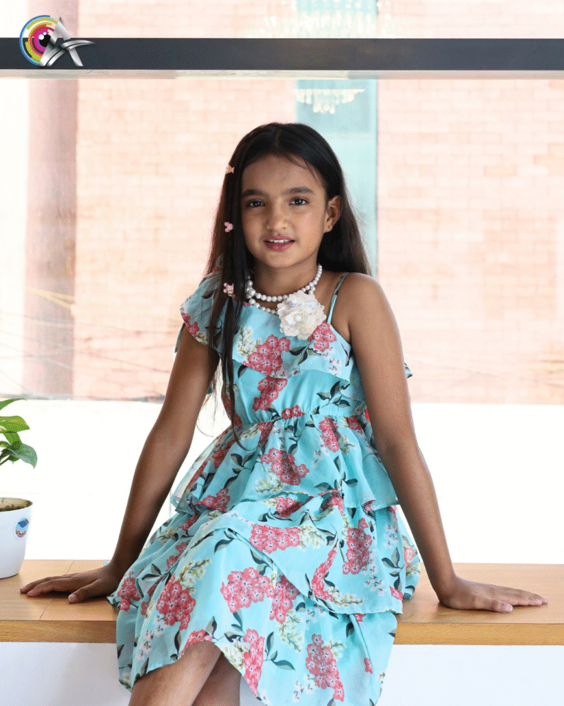 Child model in a floral outfit with long hair and hair clips, looking at the camera