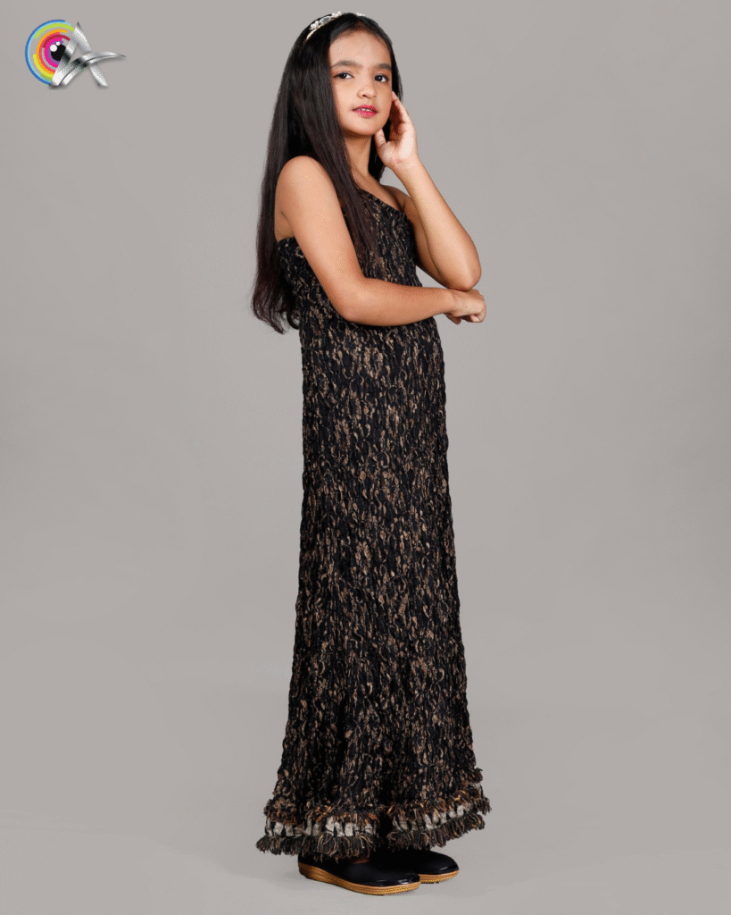 Kids fashion model in a designer black and gold gown, striking a graceful sideways pose for a professional photoshoot.
