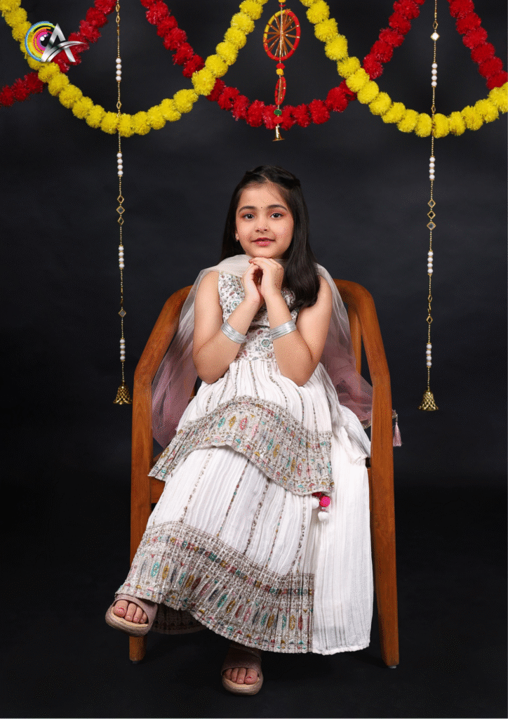 Cute little girl dressed in a white ethnic salwar suit, standing against a plain background.