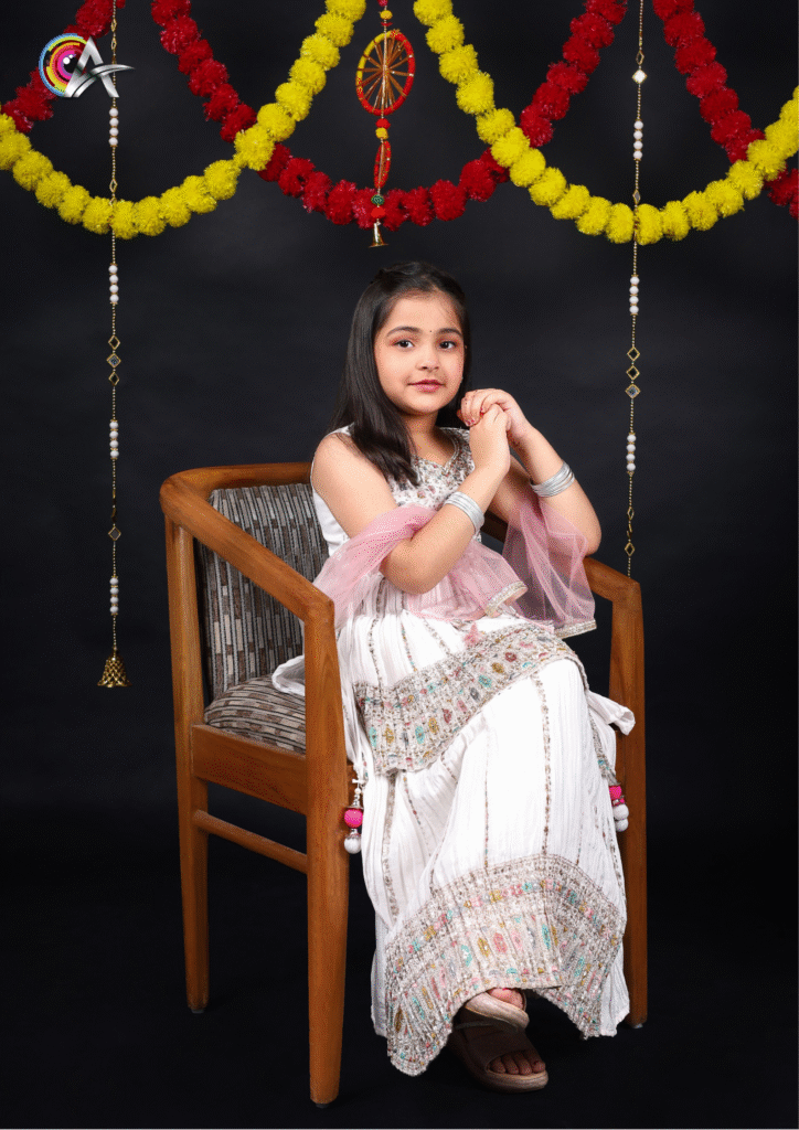Adorable child model in a white designer kurta set with dupatta, posing with folded hands.