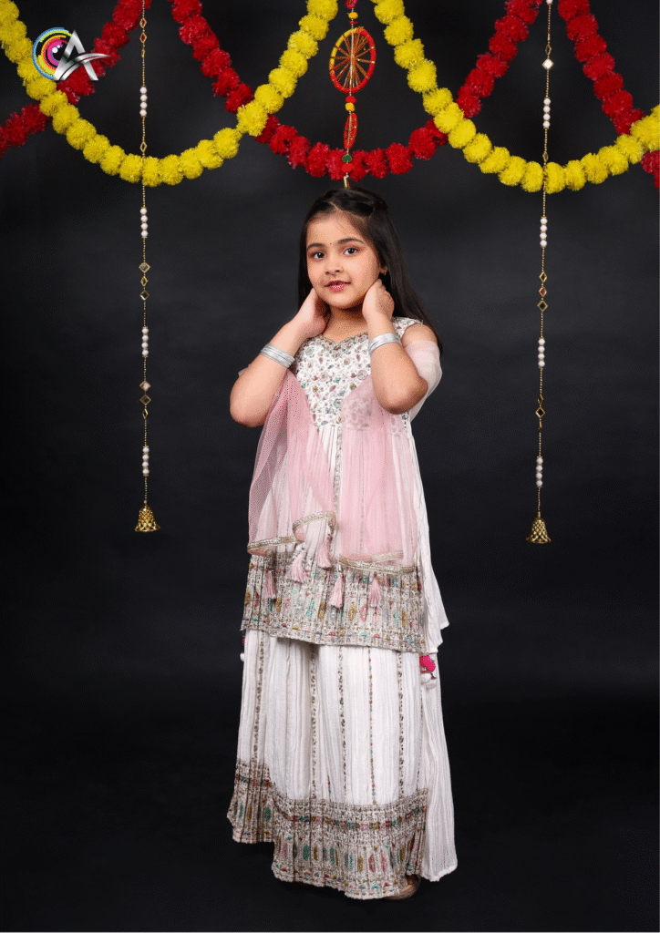 Girl in white traditional attire posing confidently in studio lighting for kidswear photography.