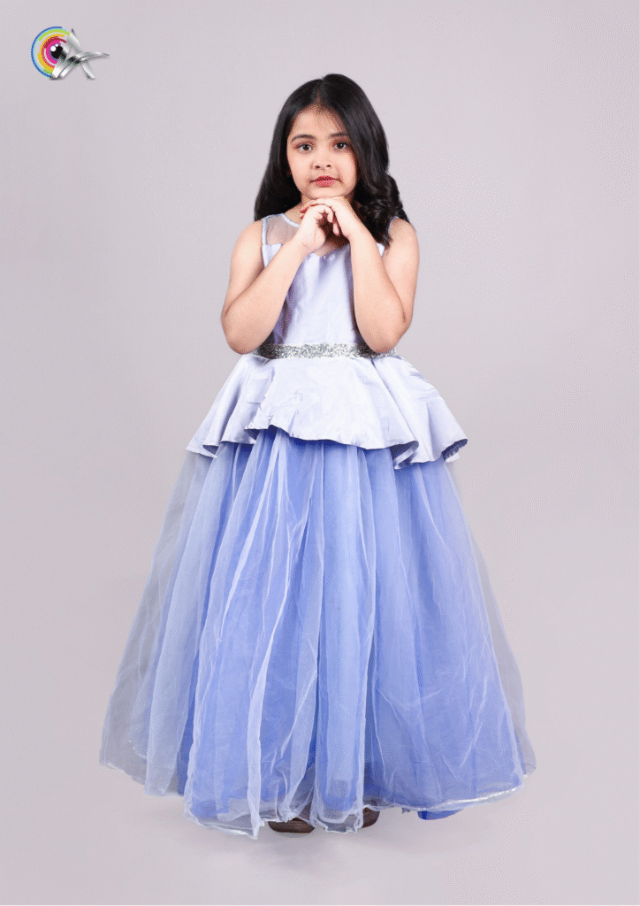 Cute young girl wearing a sleeveless blue frock with a layered tulle skirt, standing with folded hands.
