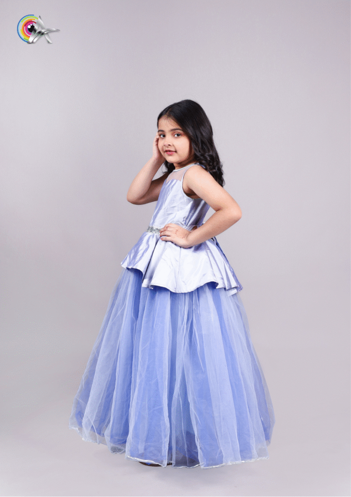 Pretty girl model in a blue evening gown smiling slightly, standing on a plain backdrop.