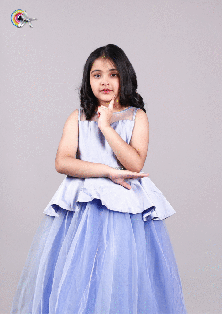 Child wearing a flowy light blue gown with layered net design, posing confidently indoors.