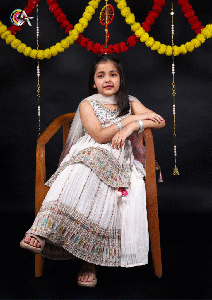Young girl wearing a traditional white suit with elegant detailing, posing gracefully in a studio.
